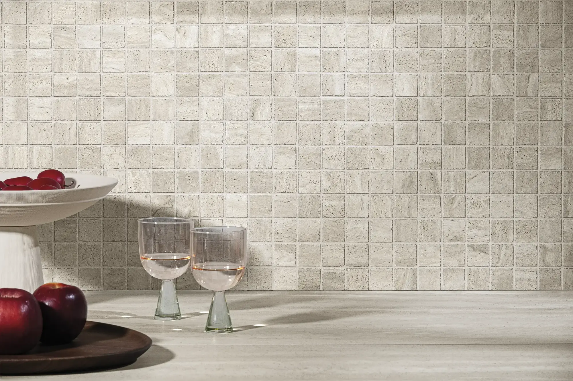 Aeterna Taupe tile wall with two crystal glasses and fresh fruits on black side table – warm tone interior